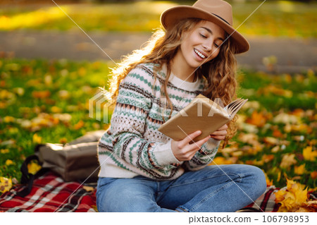 Beautiful curly woman in hat on mat with book in autumn park. Relaxation, solitude with nature. Beautiful curly woman in hat on mat with book in autumn park. Relaxation, solitude with nature. 106798953
