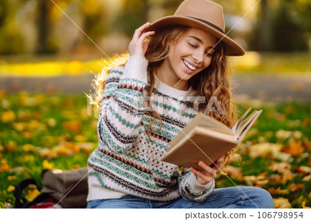 Beautiful curly woman in hat on mat with book in autumn park. Relaxation, solitude with nature. Beautiful curly woman in hat on mat with book in autumn park. Relaxation, solitude with nature. 106798954