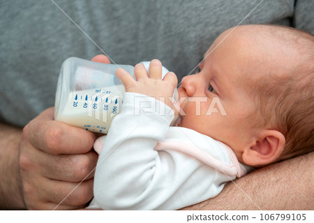 Father's love shines, man holding and feeding his newborn with nourishing formula 106799105