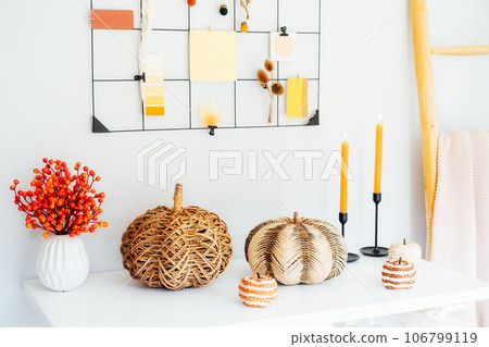Cozy autumn home interior decor- various decorative wicker pumpkins, candles, seasonal flowers in vase on the white table with mood board with fall colors palette notes on the wall. Mood inspiration 106799119