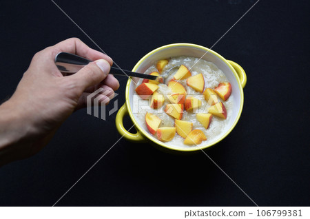oatmeal cooked in milk with pieces of ripe peach in a bowl on a black background 106799381