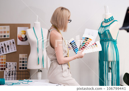 Woman fashion designer with color swatch and outfit sketch works in clothes atelier craft macrame dress on mannequin in sewing workshop creative dressmaker in workshop 106799441