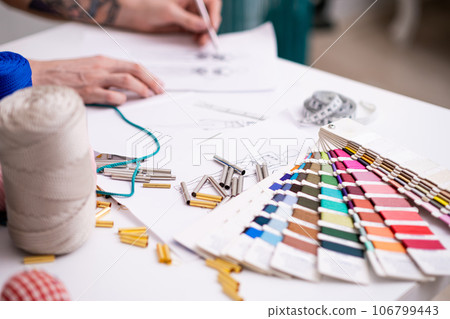 Color swatch palette and small metal tubes on tailor desk in sewing atelier dressmaker draws outfit model sketch in craft dressmaking workshop closeup 106799443