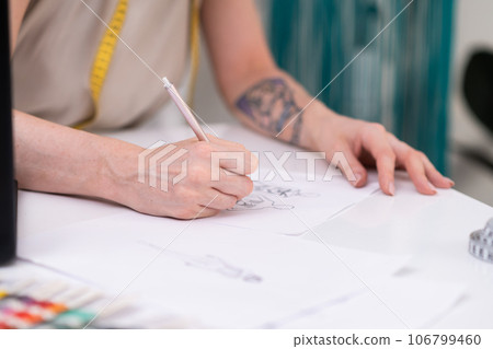 Woman draws dress model sitting at desk in clothes atelier talented designer makes sketch of stylish apparel for women in fashion studio closeup sewing industry 106799460