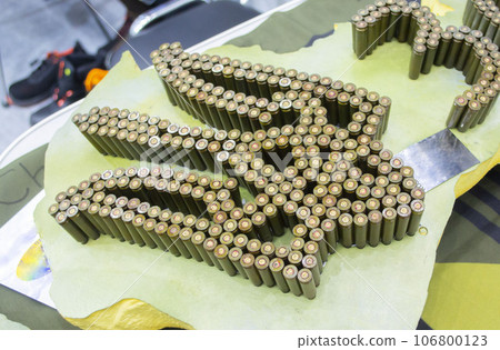 Emblem, coat of arms of Ukraine trident from used cartridges. Object made up of spent used cartridge cases. Lots used shells from cartridge cases ammo close up. Model from Many Used cartridge Cases. Emblem, coat of arms of Ukraine trident from used cartridges. Object made up of spent used cartridge cases. Lots used shells from cartridge cases ammo close up. Model from Many Used cartridge Cases. 106800123