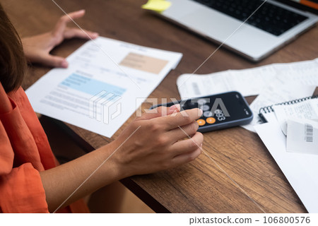 A lady, armed with payment receipts, pays household utility bills online from home using her trusty laptop A lady, armed with payment receipts, pays household utility bills online from home using her trusty laptop 106800576