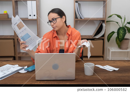 At home, a woman efficiently handles household utility bills online, laptop as her tool, clutching payment receipts securely 106800582
