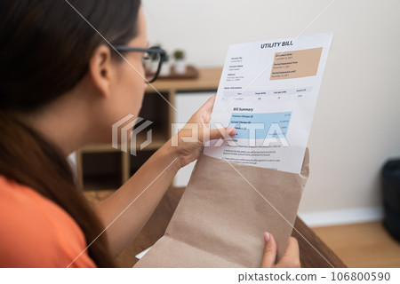 Financial Inspection: Holding an envelope, a woman meticulously reviews a utility bill, painting a vivid picture of taxes and household expenses 106800590
