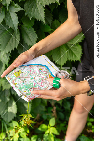 Woman holding a map and the compass during orienteering competitions. Woman holding a map and the compass during orienteering competitions. 106801035