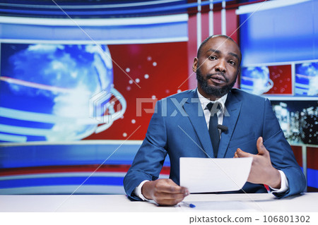 Presenter delivering news from papers headlines, reporting exclusive information about latest events worldwide. African american news anchor transmitting details about business or politics. Presenter delivering news from papers headlines, reporting exclusive information about latest events worldwide. African american news anchor transmitting details about business or politics. 106801302