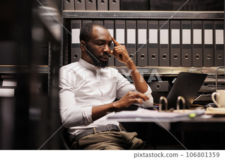 African american detective solving complex crime case using laptop. Law enforcement professional thinking about evidence and checking proofs on computer in police office room 106801359