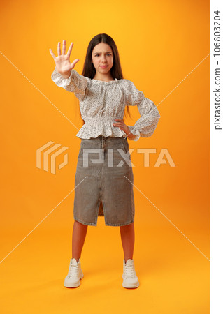 Teen girl extend hand in block gesture against yellow background Teen girl extend hand in block gesture against yellow background 106803204