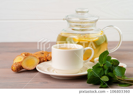 Cup of tea with ginger and mint on wooden table 106803360