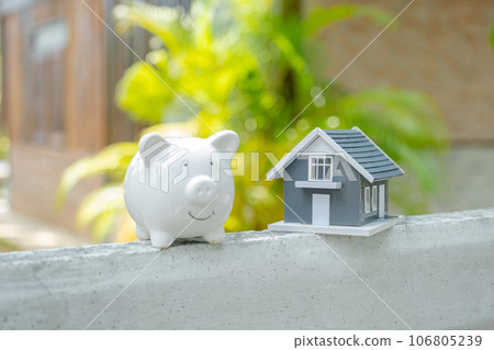 piggybank and the home model stands in front of home background, Saving money for buy real Estate concept piggybank and the home model stands in front of home background, Saving money for buy real Estate concept 106805239