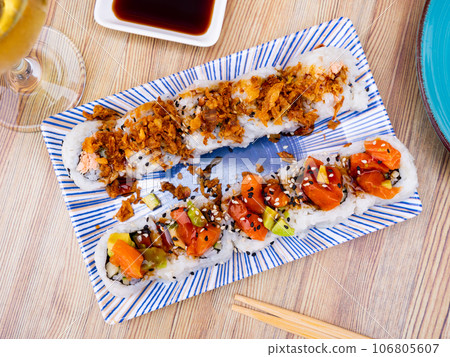 On table there is plate with set of sushi - uramaki rolls with cucumber, avocado crab and salmon On table there is plate with set of sushi - uramaki rolls with cucumber, avocado crab and salmon 106805607