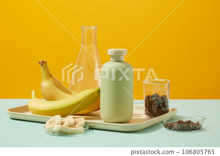 Against the yellow background, a green bottle decorated with bananas and coffee beans contained on lab glassware. Beauty product packaging design templates based on natural ingredient 106805765