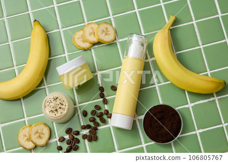 On the green ceramic background, set of cosmetic bottles displayed with ripe bananas, brown coffee beans and powder. Natural ingredients for cosmetics of skin care. Top view 106805767