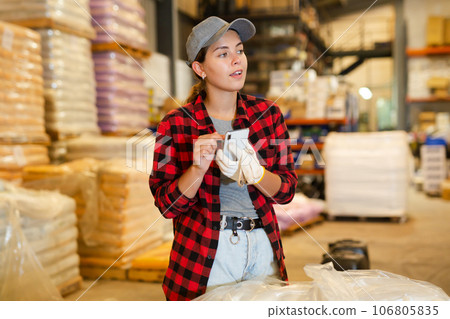 Woman checking availability on smartphones in storage warehouse Woman checking availability on smartphones in storage warehouse 106805835
