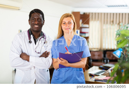 Smiling african american doctor standing in office with female assistant 106806095