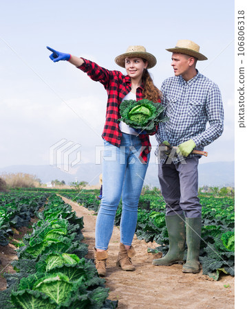 Positive couple of farmers woman and man standing at farm field 106806318