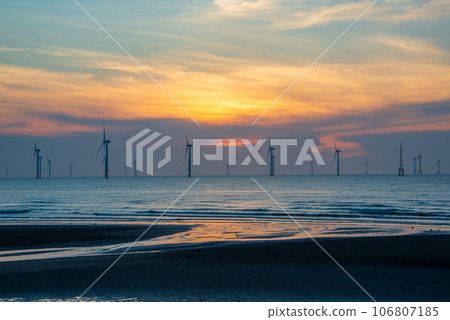 Fans of wind turbines spin over the sparkling sea. Dynamic clouds at sunset. 106807185