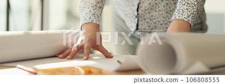 Female designer is standing near her work desk with rolls of paper. Female designer is standing near her work desk with rolls of paper. 106808555