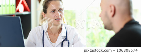 Female doctor listens attentively to patient's story about his illness, sitting at hospital table. 106808574