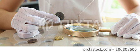 Numismatist in white gloves examines ancient coins collection at table. Numismatist in white gloves examines ancient coins collection at table. 106808606