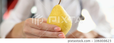 Close-up of pear in hand of nutritionist above medical office table. Close-up of pear in hand of nutritionist above medical office table. 106808623