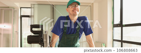 Smiling craftsman in glasses cuts board with circular saw in new office building. Smiling craftsman in glasses cuts board with circular saw in new office building. 106808663