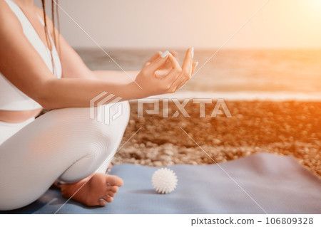 Close up Yoga Hand Gesture of Woman Doing an Outdoor meditation. Blurred sea background. Woman on yoga mat in beach meditation, mental health training or mind wellness by ocean, sea. Selective focus Close up Yoga Hand Gesture of Woman Doing an Outdoor meditation. Blurred sea background. Woman on yoga mat in beach meditation, mental health training or mind wellness by ocean, sea. Selective focus 106809328
