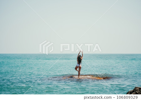 Woman sea yoga. Back view of free calm happy satisfied woman with long hair standing on top rock with yoga position against of sky by the sea. Healthy lifestyle outdoors in nature, fitness concept 106809329