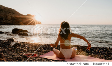 Woman sea yoga. Happy woman in white swimsuit and boho style braclets practicing outdoors on yoga mat by sea on sunset. Women yoga fitness routine. Healthy lifestyle, harmony and meditation 106809331