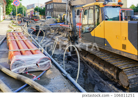 Street reconstruction view, deep and wide trench, replaced pipes and wells, new pipes, excavator Street reconstruction view, deep and wide trench, replaced pipes and wells, new pipes, excavator 106811251