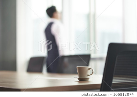 asian businessman standing in front of office window thinking, hands in pockets, focus on foreground 106812074