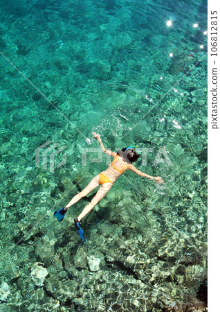 Young woman in swimsuit snorkeling in clear shallow tropical sea over coral reefs 106812815