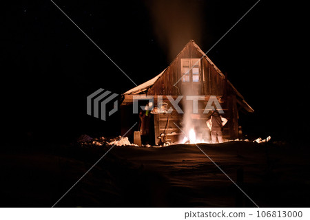 Tourist heated by fire at winter near a wooden hut Tourist heated by fire at winter near a wooden hut 106813000