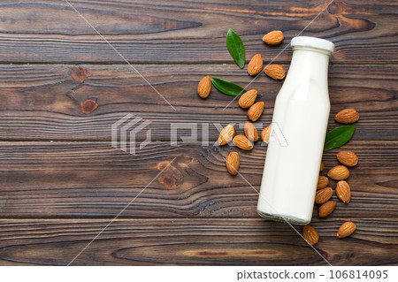 Top view of the almond milk in the glass bottle with almond nuts on the colored table. top view vith copy space Top view of the almond milk in the glass bottle with almond nuts on the colored table. top view vith copy space 106814095