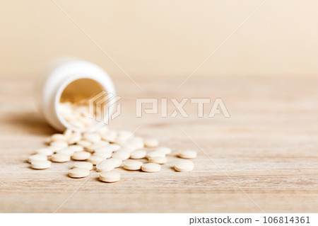 Medicine bottle and white pills spilled on a light background. Medicines and prescription pills flat lay background. White medical pills and tablets spilling out of a drug bottle Medicine bottle and white pills spilled on a light background. Medicines and prescription pills flat lay background. White medical pills and tablets spilling out of a drug bottle 106814361