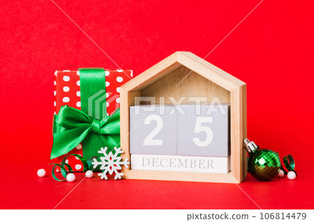 25 december. Christmas composition on colored background with a wooden calendar, with a gift box, toys, bauble copy space 25 december. Christmas composition on colored background with a wooden calendar, with a gift box, toys, bauble copy space 106814479