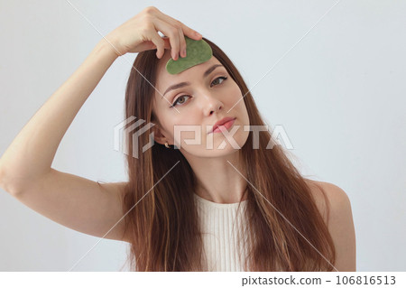 Close-up portrait of a beautiful girl, red-haired woman massaging her face with a stone scraper Close-up portrait of a beautiful girl, red-haired woman massaging her face with a stone scraper 106816513