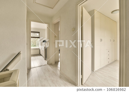 a hallway with white walls and wood flooring on the left side of the room, there is an open door leading to another a hallway with white walls and wood flooring on the left side of the room, there is an open door leading to another 106816982