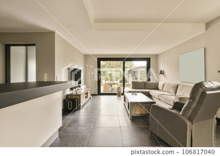 a living room with tile flooring and white walls, there is an open door leading to the patio area a living room with tile flooring and white walls, there is an open door leading to the patio area 106817040