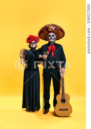 Halloween Family. Parents, father and mother in spooky makeup celebrating halloween with glasses of cocktails against yellow studio background. Halloween Family. Parents, father and mother in spooky makeup celebrating halloween with glasses of cocktails against yellow studio background. 106817800