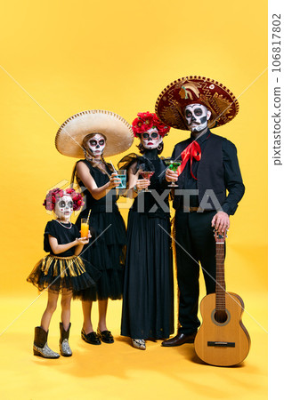 Halloween Family. Father, mother and children in spooky makeup celebrating halloween with glasses of cocktails against yellow studio background. Halloween Family. Father, mother and children in spooky makeup celebrating halloween with glasses of cocktails against yellow studio background. 106817802