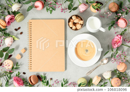 White cup of coffee, empty notebook and Frame made of Spring flowers and different types of macaroons 106818096