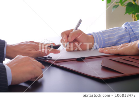 A woman filling out documents and a man prompting her to do so. 106818472