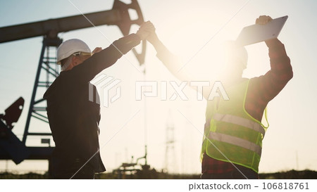 handshake business oil contract. handshake a worker and businessman shaking hands against backdrop of an oil pump. oil extraction business concept. silhouette handshake sunlight business contract 106818761