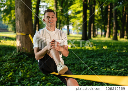 Young smiling man in the forest practising slacklining Young smiling man in the forest practising slacklining 106819569
