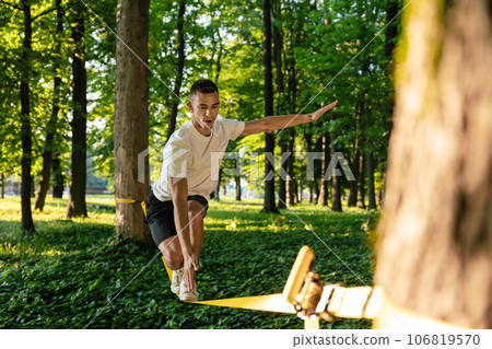 Sportsman on the rope practising slacklining and looking concentrated Sportsman on the rope practising slacklining and looking concentrated 106819570